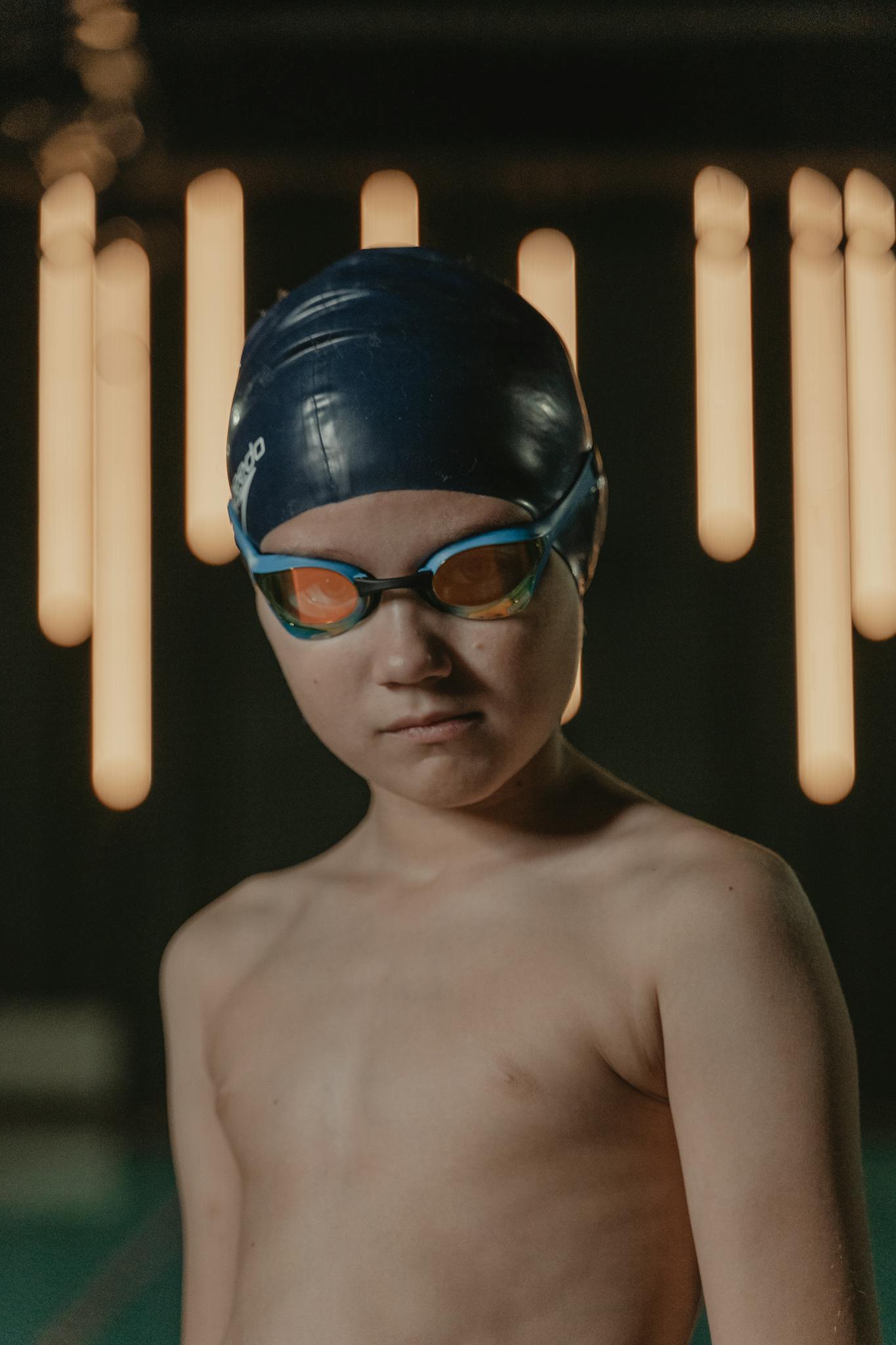 A determined young swimmer with goggles and swim cap in an indoor pool setting.